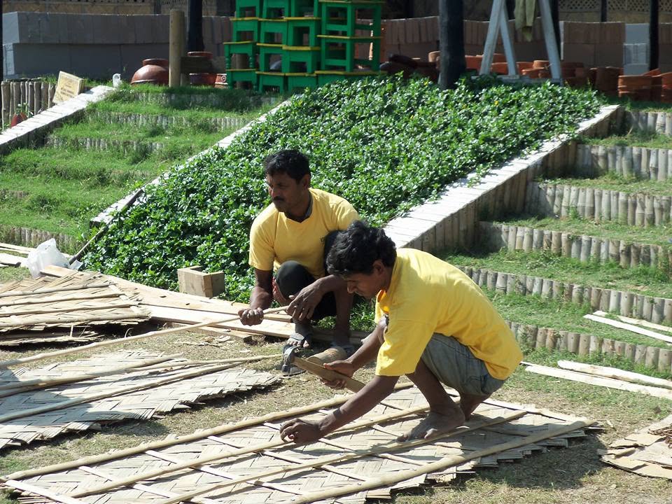 Two karigars weaving bamboo lattice panels on the grass